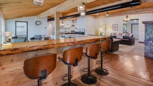 Una habitación amplia con techo de madera, una zona de bar central con taburetes y una chimenea de piedra.