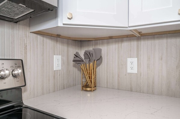 A kitchen with a white countertop, a built-in stove, and a gold utensil holder. - Covington Charm 202 (Covington)