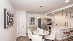 Une cuisine moderne dotée d’un îlot central, d’appareils électroménagers en acier inoxydable et de luminaires suspendus.