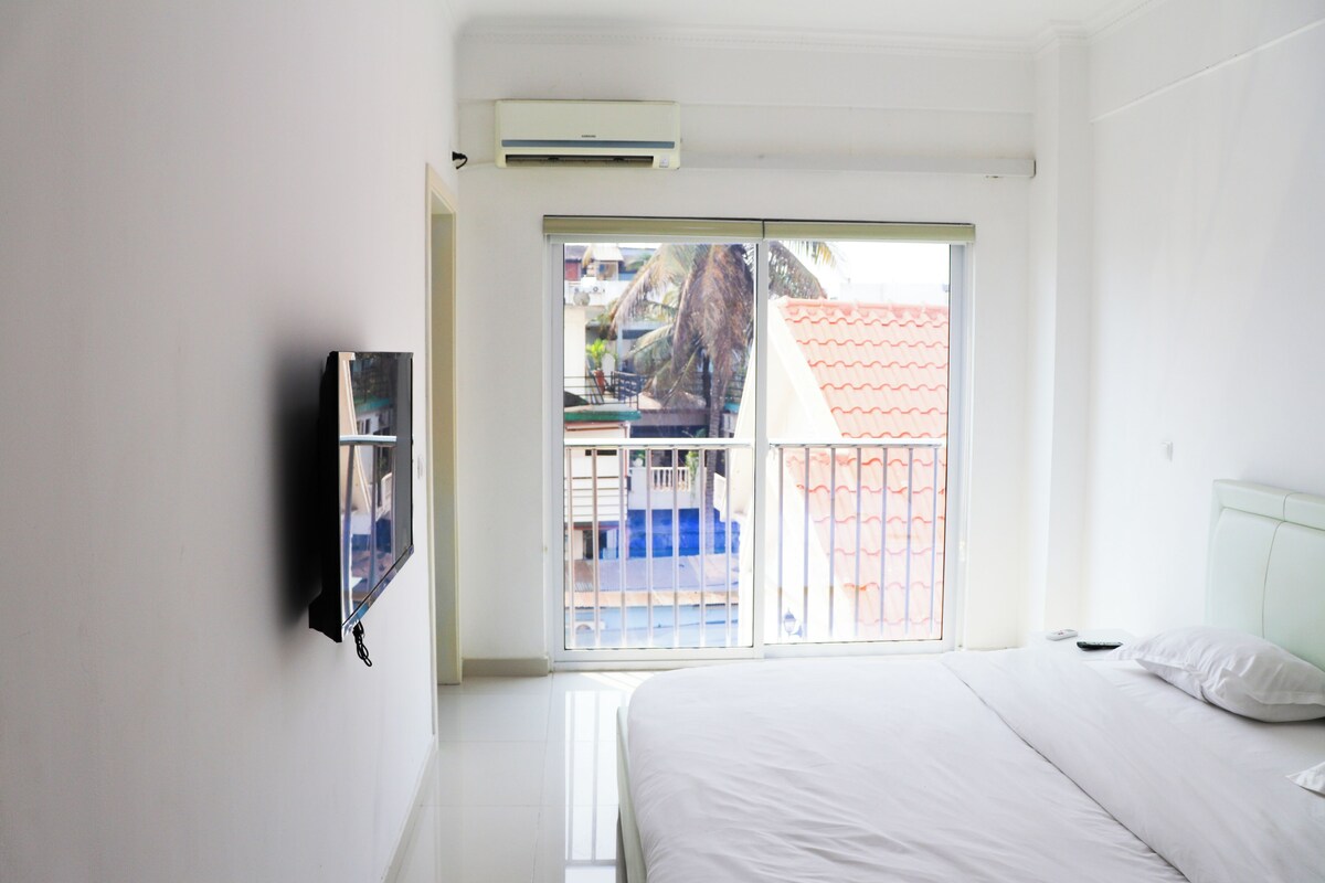 A hotel room with a bed, a TV mounted on the wall, and a sliding glass door leading to an outdoor area.