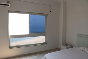 A bedroom with a bed, a nightstand, a phone, and a window with a beach view. - Hotel Coral da Ilha (Luanda)