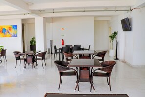 A spacious dining area with a large table and multiple chairs, a fire extinguisher on the wall, and a potted plant. - Hotel Coral da Ilha (Luanda)