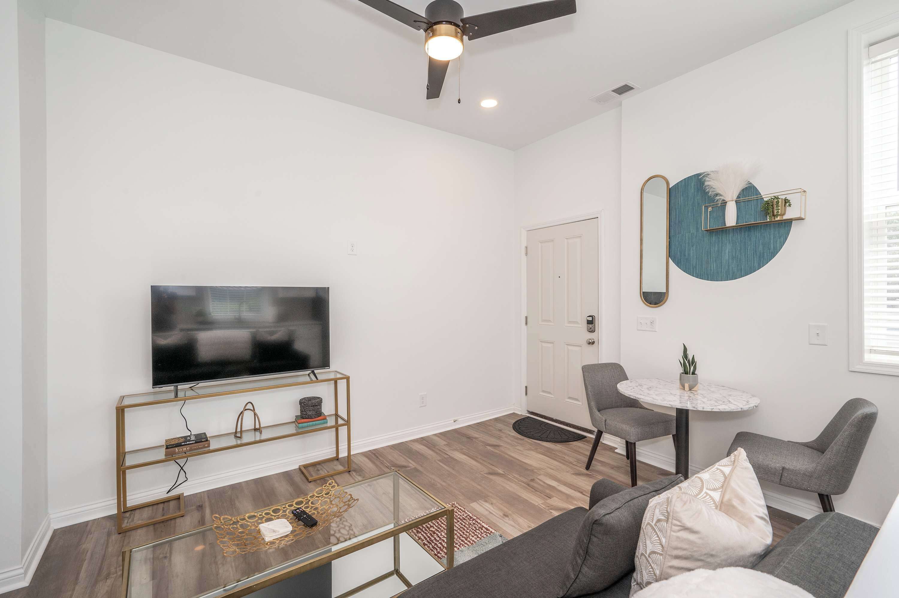 A modern living room with a flat-screen TV, a round coffee table, a sofa, and a dining table with chairs.