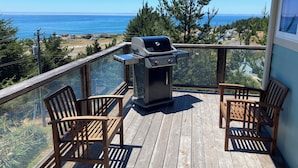 Una terraza de madera con una parrilla y dos sillas, con vista al mar.