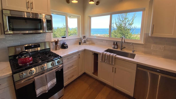 Una cocina moderna con electrodomésticos de acero inoxidable, armarios blancos y grandes ventanales con vistas al océano.