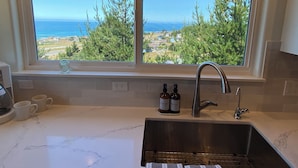 Una cocina con un amplio ventanal que ofrece una vista panorámica del océano y los árboles.