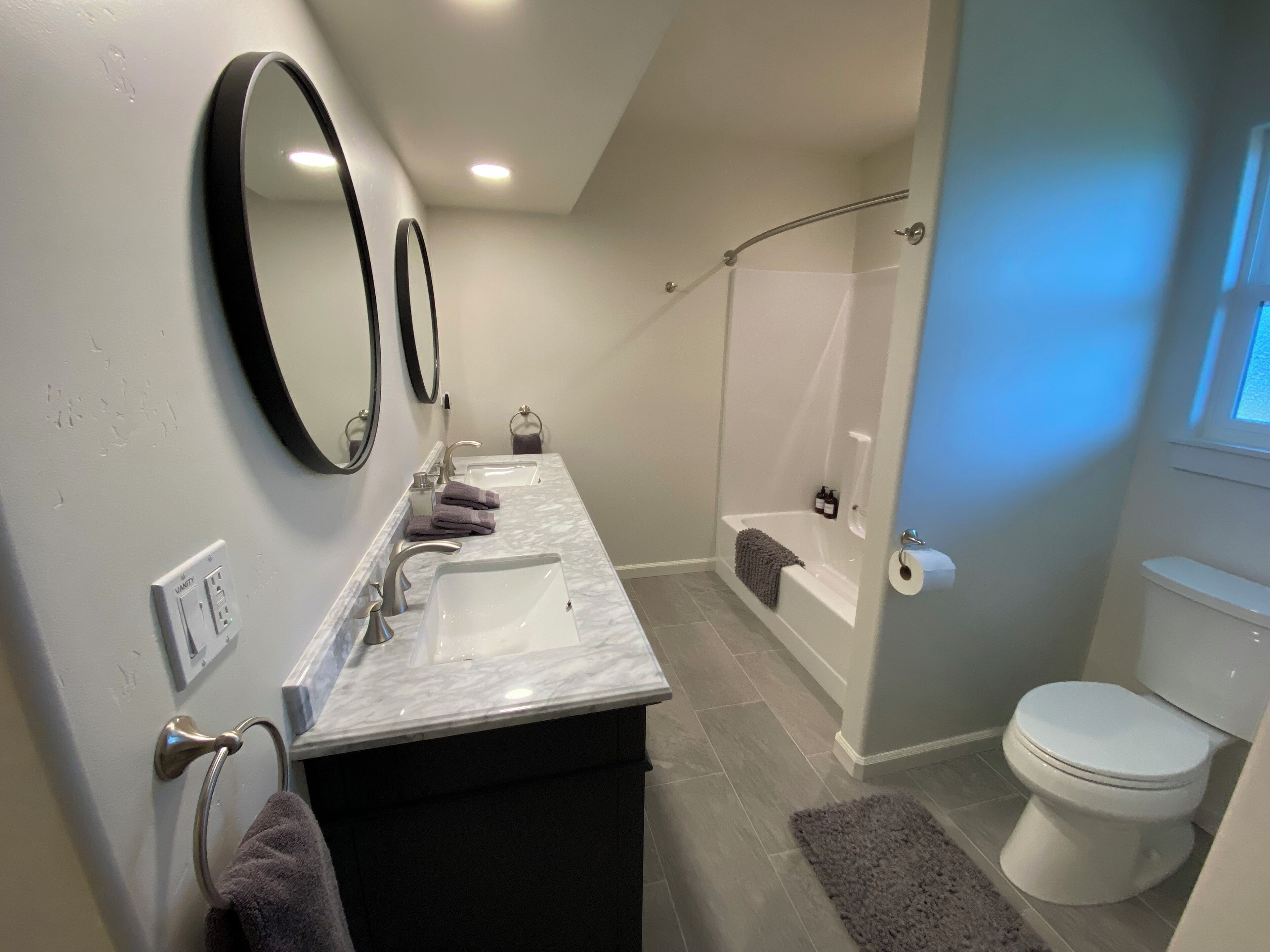A modern bathroom with a marble vanity, two sinks, a shower, and a toilet.