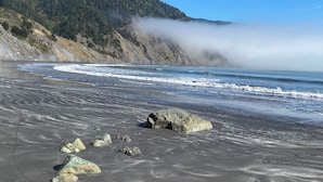 Una playa con un primer plano rocoso y un cerro boscoso al fondo.