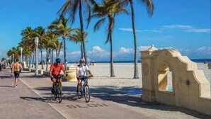 A beachside walkway with palm trees, cyclists, and a clear blue sky. - Private Parking + Own Patio
+ FREE Bikes 1b/1b Apt (Hollywood)