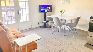 A modern living room with a sofa, a small table, a TV, and a dining area with chairs and a vase of flowers. - Private Parking + Own Patio
+ FREE Bikes 1b/1b Apt (Hollywood)