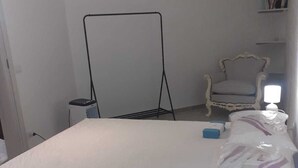 Een slaapkamer met een bed, een nachtkastje, een stoel en een vloerlamp.