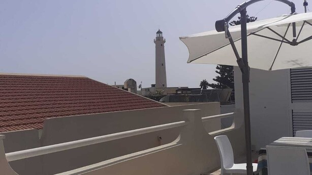 Een dakterras met een tafel, stoelen, een witte parasol en een vuurtoren op de achtergrond.