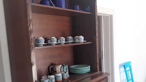 Een houten kast met planken en lades, gevuld met diverse keukenbenodigdheden zoals borden, kommen en bekers.