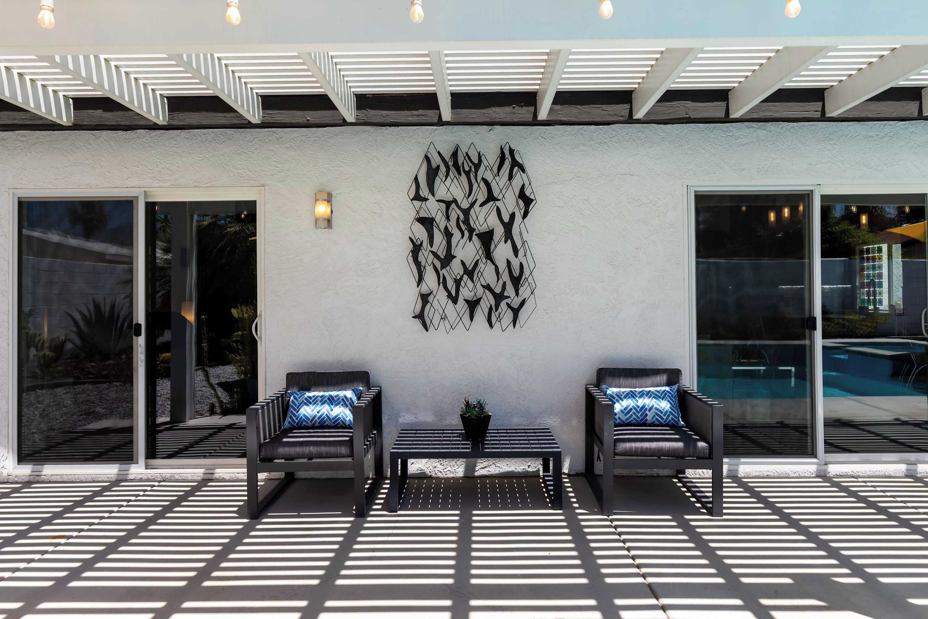 An outdoor patio with two black leather sofas, a central table, and a wall-mounted abstract art piece.