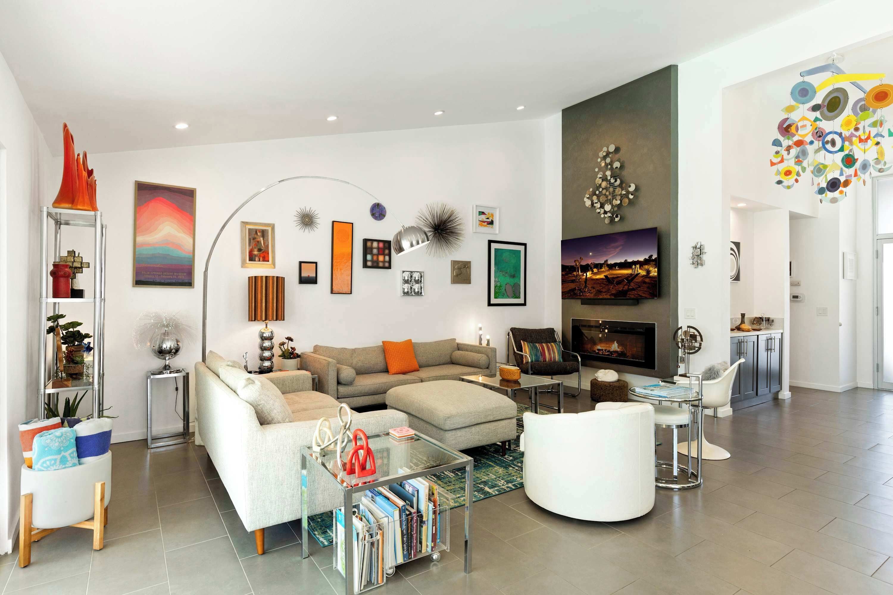 A modern living room with a sofa, ottoman, coffee table, and a fireplace. There are wall art pieces and a decorative ceiling light.