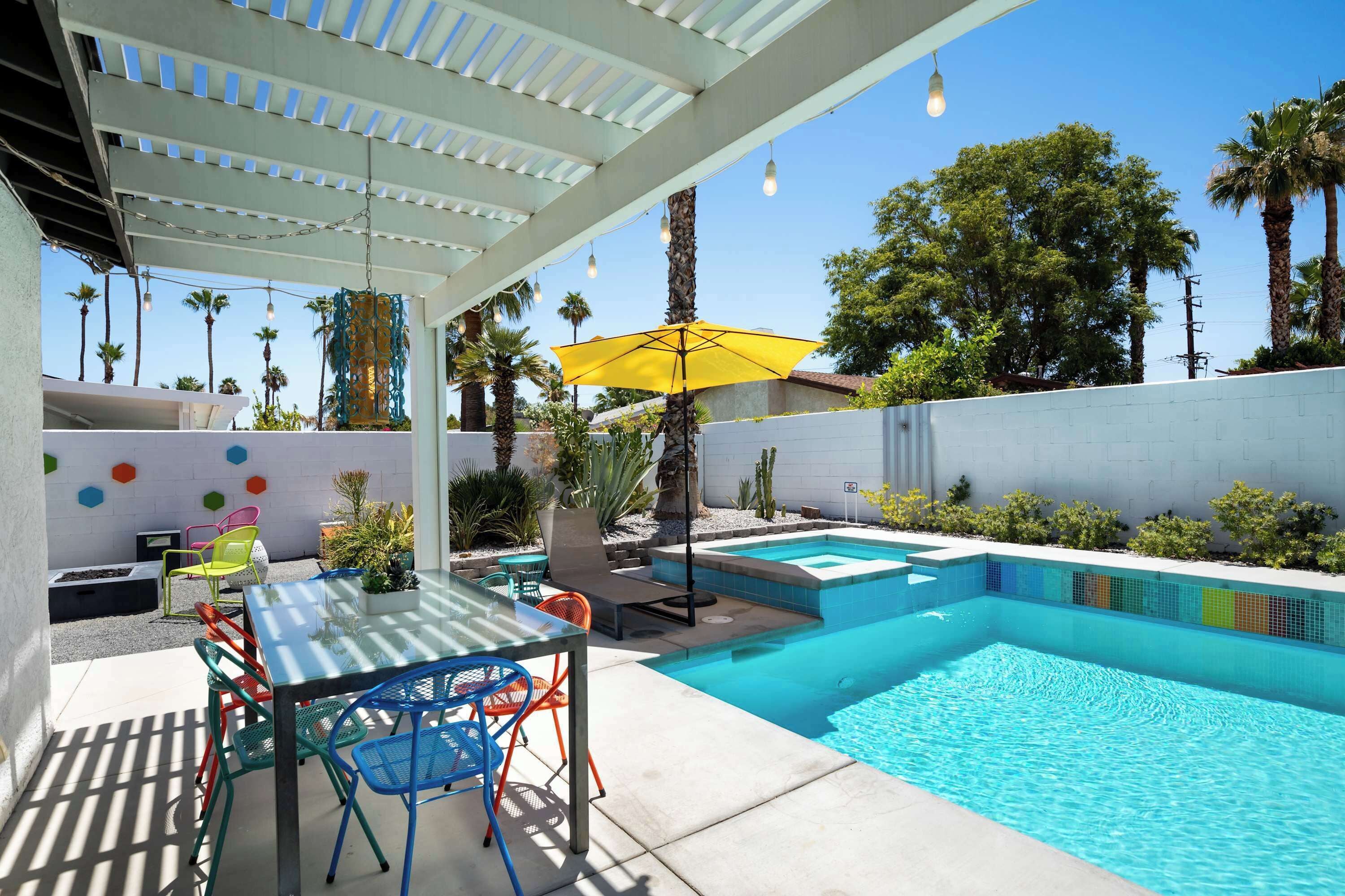 Um quintal com piscina, móveis de pátio e uma pérgola com luzes penduradas.
