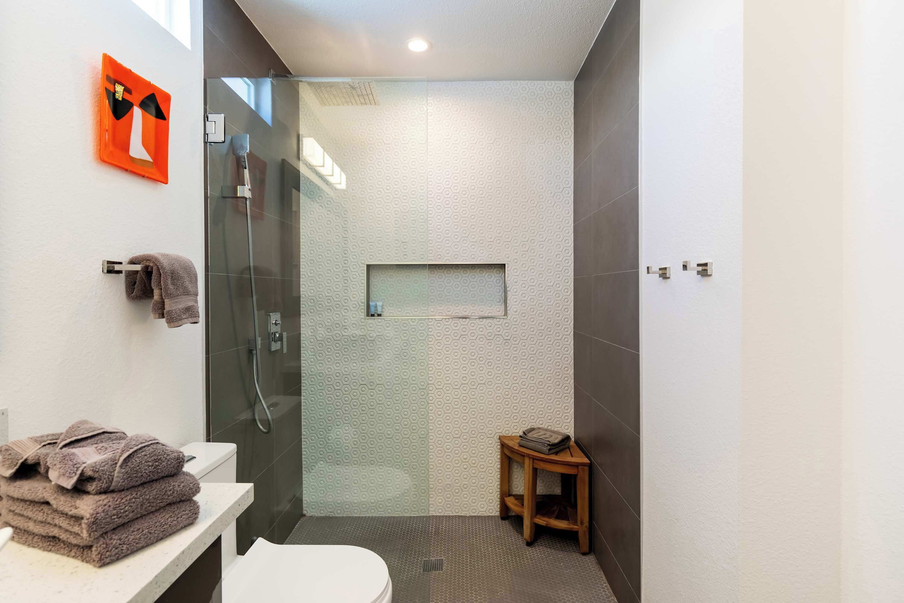 A modern bathroom with a glass-enclosed shower, a toilet, and a sink with towels.