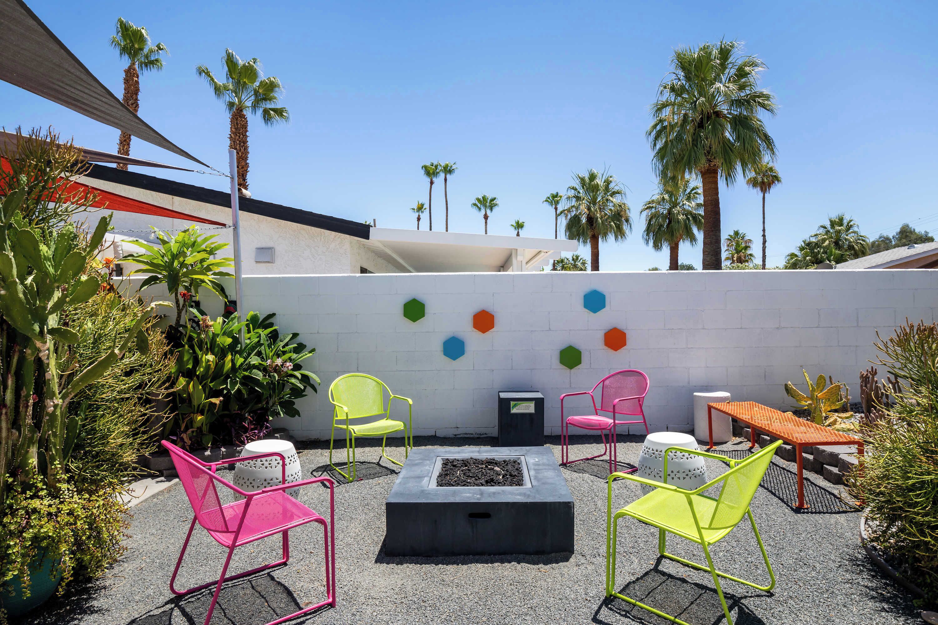 An outdoor patio with colorful chairs, a fire pit, and a white wall with hexagonal decorations.