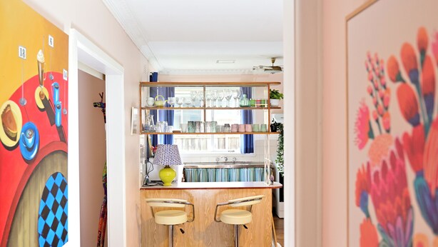 Una cocina con encimera de madera, dos taburetes de bar y una estantería con cristalería.