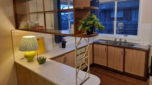 Una cocina con armarios de madera, una encimera blanca, una lámpara amarilla y una ventana que da a un patio trasero.