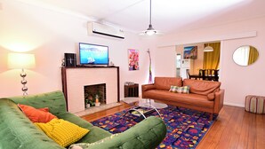 Una sala de estar con un sofá verde, un sofá marrón, una chimenea, un televisor y un tapete colorido.