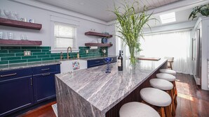 A modern kitchen with dark blue cabinets, a marble island, and a bar area with stools.