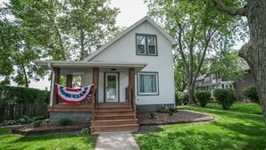 A single-story house with a front porch, a small garden, and a flag.