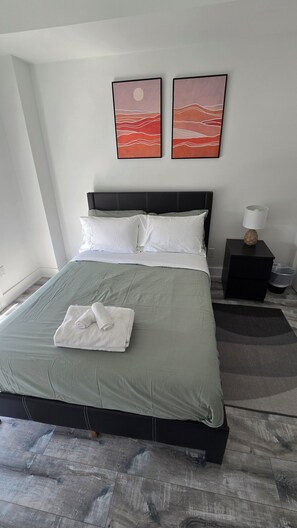 A neatly made bed with a green bedspread, white pillows, and a folded towel. There are two framed artworks on the wall above the bed.