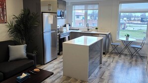 A modern kitchen with a central island, a dining area with a table and chairs, a sofa, and a large window providing a view of the outside. - Minutes To The Falls:  Stylish Townhome Gem! (Niagara Falls)