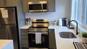 A modern kitchen with stainless steel appliances, a built-in oven, and a large window providing natural light. - Minutes To The Falls:  Stylish Townhome Gem! (Niagara Falls)