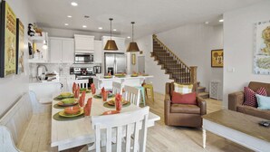A modern kitchen with white cabinets, a dining area with a wooden table set for four, and a staircase leading to another level. - Live in Fantasy at Disney in the Desert! (Washington)