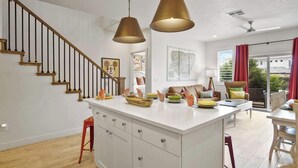 A modern kitchen with a central island, wooden staircase, and a dining area with red curtains. - Live in Fantasy at Disney in the Desert! (Washington)