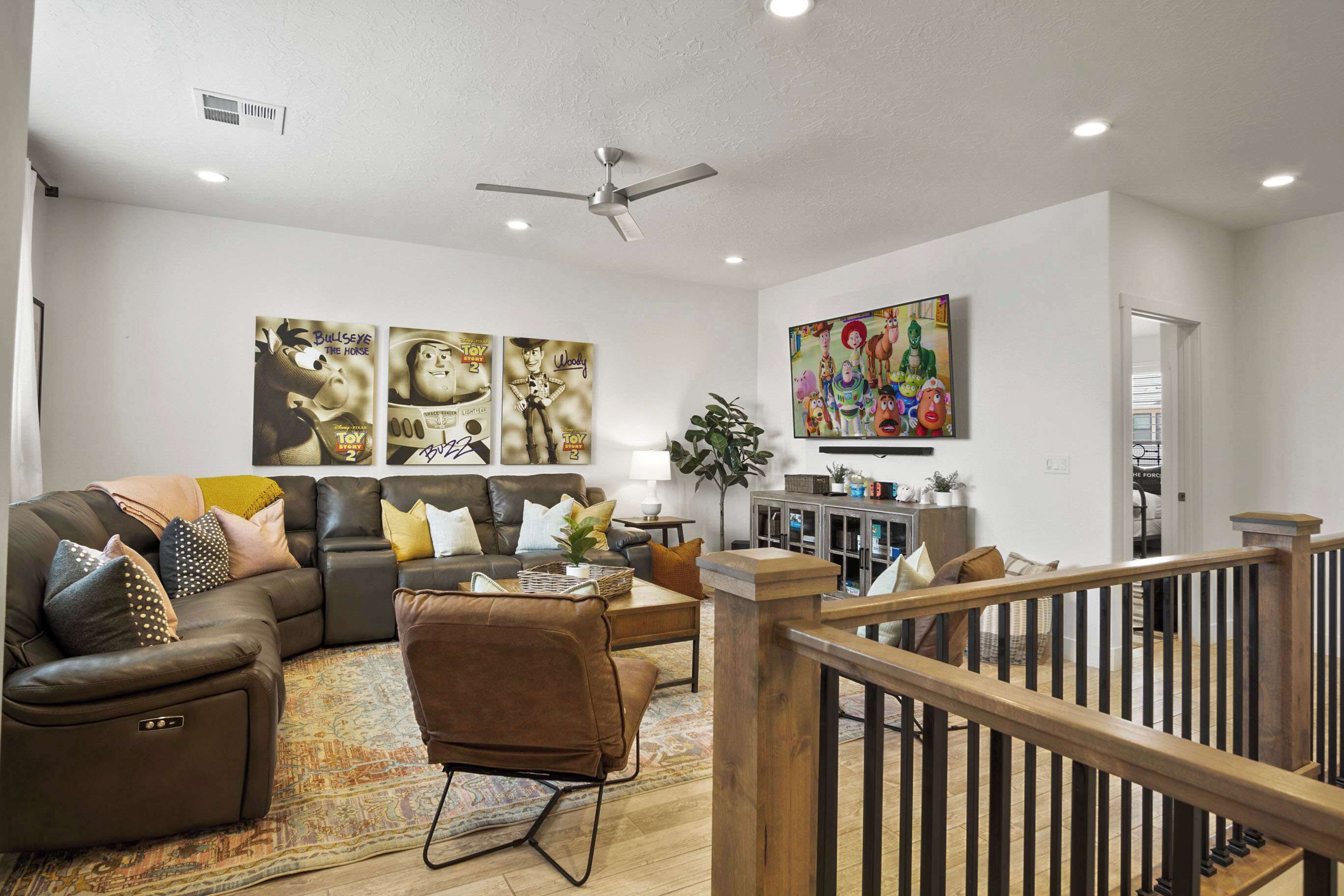 A modern living room with a sectional sofa, a coffee table, and a TV. There is a ceiling fan, a plant, and artwork on the walls.