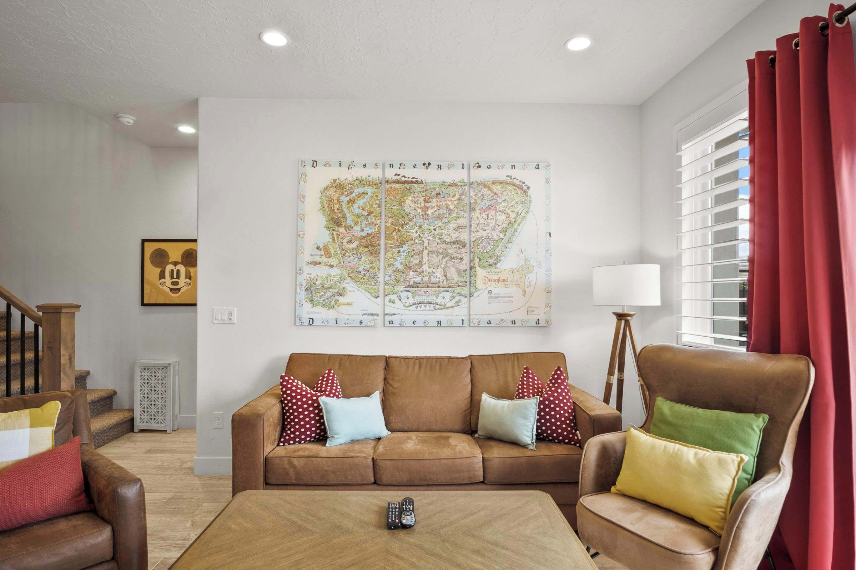 Ein Wohnzimmer mit einem braunen Sofa, roten und weißen Kissen mit Punkten, einem Holztisch und einer Karte von Disneyland an der Wand.