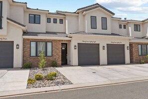 A row of townhouses with individual garage doors, a small landscaped area with rocks and plants, and a clear sky.