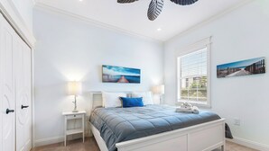A bedroom with a bed, nightstands, a window, and artwork on the walls.