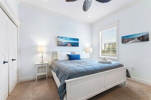 Une chambre à coucher avec un lit, deux tables de chevet, une fenêtre et des œuvres d’art accrochées aux murs.