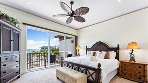 A bedroom with a large bed, a wooden dresser, a bench, and a ceiling fan.