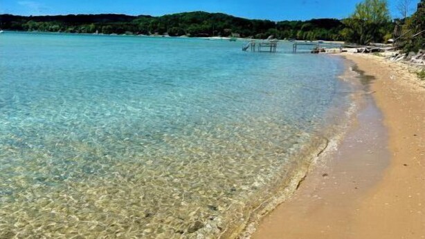 A clear beach with shallow water, a sandy shore, and a distant pier.