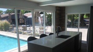Una cocina moderna con una isla grande, un lavamanos integrado y vistas a una piscina y mobiliario de patio.