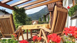 A wooden outdoor seating area with a table and chairs, surrounded by red flowers and greenery, with a mountain view in the background. - Rätia I by Interhome (Pfunds-Samnaun)