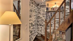 A staircase with a stone wall and wooden steps, leading to a bookshelf. - Le Gîte de Gravelodic (PAIMPOL)