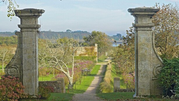 A pathway leading through a garden with stone pillars and a view of the countryside. - Le Gîte de Gravelodic (PAIMPOL)