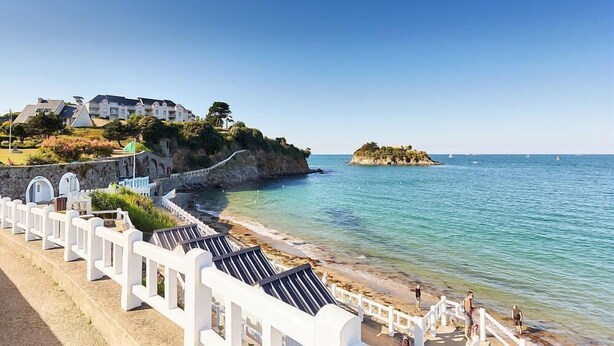 Ein Küstenhotel mit Blick auf einen Strand, eine felsige Klippe und eine kleine Insel in der Ferne.