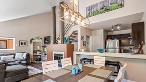 Una sala de estar moderna con chimenea, un comedor con una mesa grande y una cocina con refrigerador y armarios.
