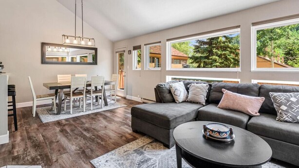 Una sala de estar moderna con un sofá modular, una mesa de comedor y sillas. Amplias ventanas ofrecen vistas al exterior.