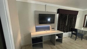 A modern room with a flat-screen TV mounted on the wall, a desk with a chair, and a window with dark curtains. - Black Horse Motel (Apple Valley)