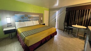 A hotel room with a bed, a desk, a chair, and a view of palm trees. - Black Horse Motel (Apple Valley)
