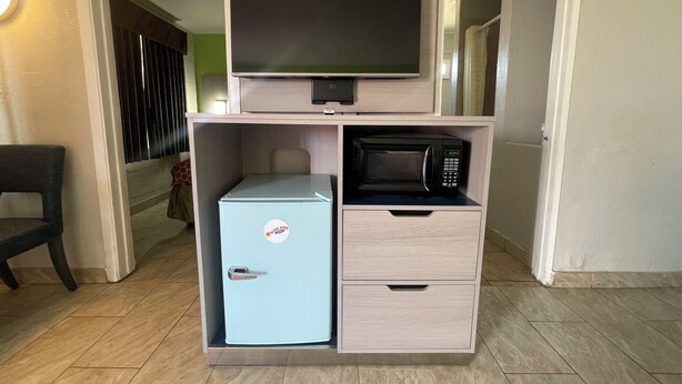 A compact kitchenette with a refrigerator, microwave, and a flat-screen TV on a wooden cabinet. - Black Horse Motel (Apple Valley)