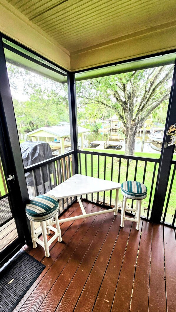 A covered porch with a table and two chairs, a view of a backyard with a tree and a house.